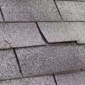 Close view of cracked and damaged asphalt shingles showing signs of aging and repair needs.