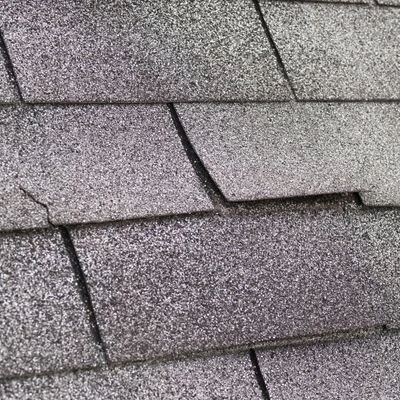 Close view of cracked and damaged asphalt shingles showing signs of aging and repair needs.
