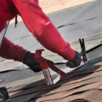 Closeup of roofer's hands using a hammer to secure a support on a roof
