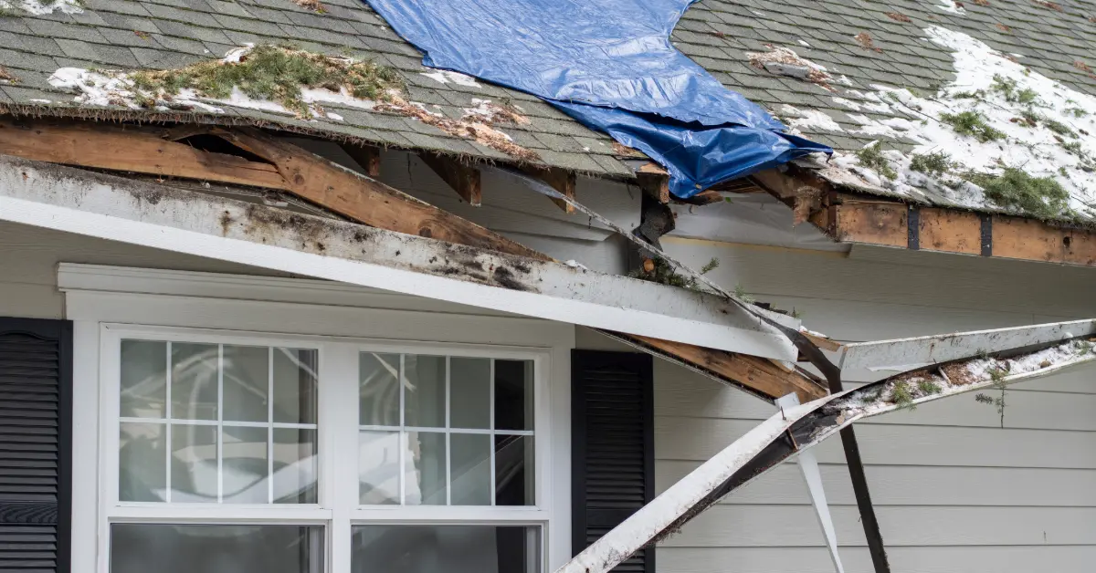 A home with a severely damaged roof with a blue tarp.