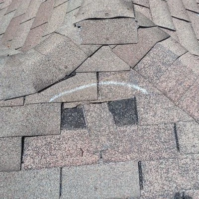 Cracked and damaged asphalt shingles on residential roof requiring emergency repair