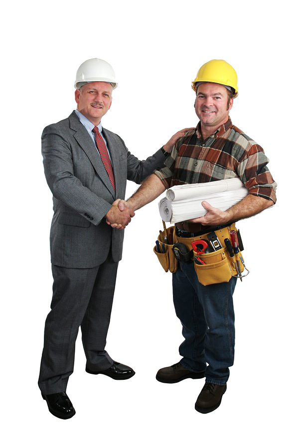 Construction professional in yellow hard hat and tool belt shaking hands with a building owner in white hard hat and business suit, representing a roofing project agreement.