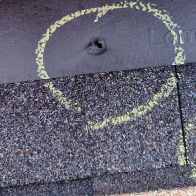 close-up of nail hole in metal and shingle on roof, which is the origination of a leak