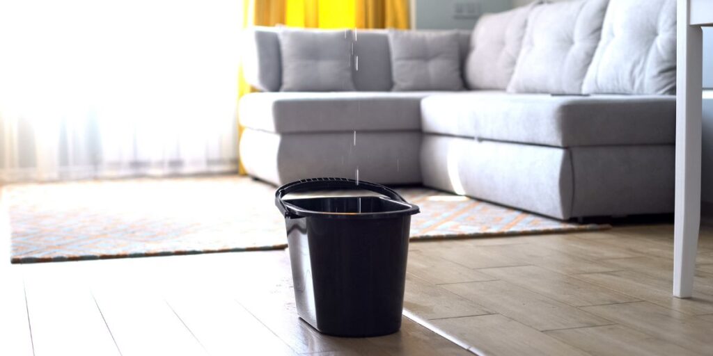 black bucket catching dropping water from roof leak