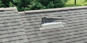 Damaged asphalt roof shingles with missing sections exposing underlayment on residential home