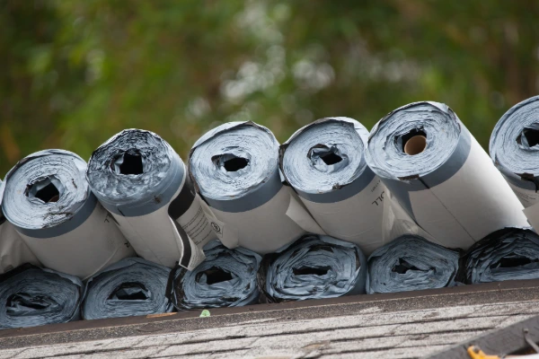 Close-up of roofing materials staged on a roof deck, showing underlayment rolls ready for installation.