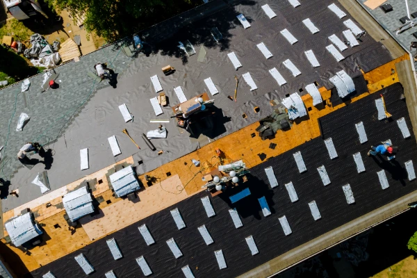 An aerial drone shot of a professional roofing crew installing synthetic underlayment and shingles on a large residential roof.