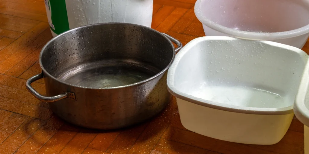 Buckets and containers placed on a floor to catch water from an active roof leak