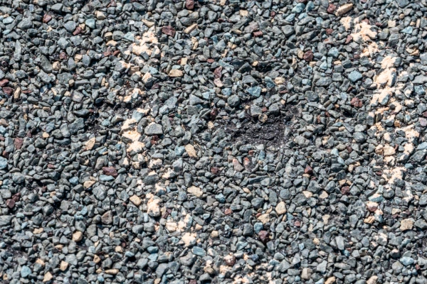 Close-up of asphalt shingle surface showing granule loss and exposed mat caused by hail impact damage.