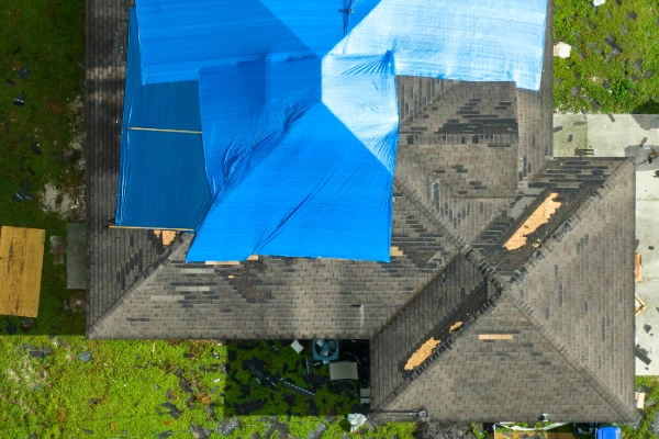 Aerial view of a damaged roof covered with a blue tarp for temporary repair